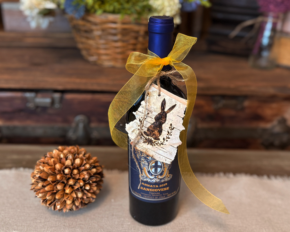 A bottle of wine with a handmade birch bark gift tag tied to the bottle with a yellow bow.